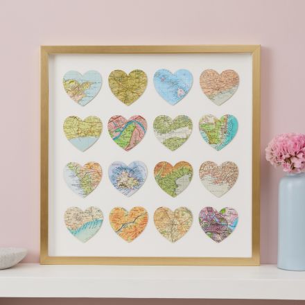 Sixteen map hearts in gold frame hung on pink wall above white mantelpiece