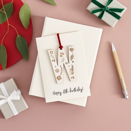 Wooden letter keepsake engraved with a name and flowers and strung on white card printed with Christmas message.