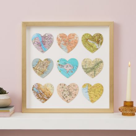 Nine map location hearts in gold frame mounted on pink wall over mantelpiece.