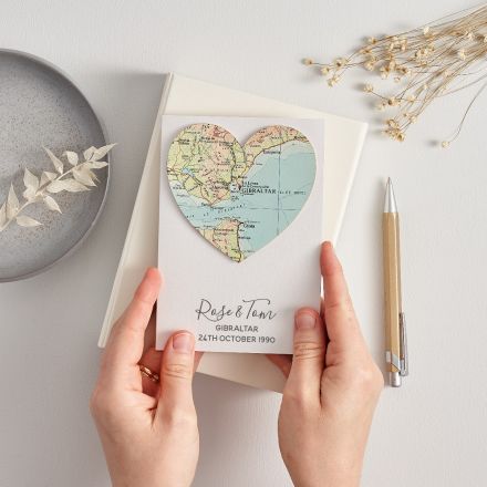 Hand holding a 30th wedding anniversary card with a map heart, dried flowers and a gold pen