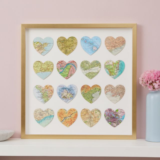 Sixteen map hearts in gold frame hung on pink wall above white mantelpiece