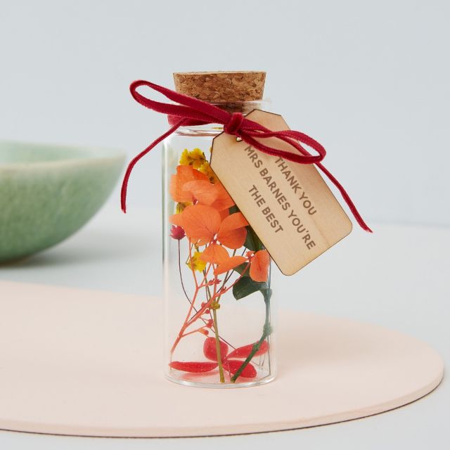 Miniature glass bottle holding delicate dried flowers and wooden tag with own message.