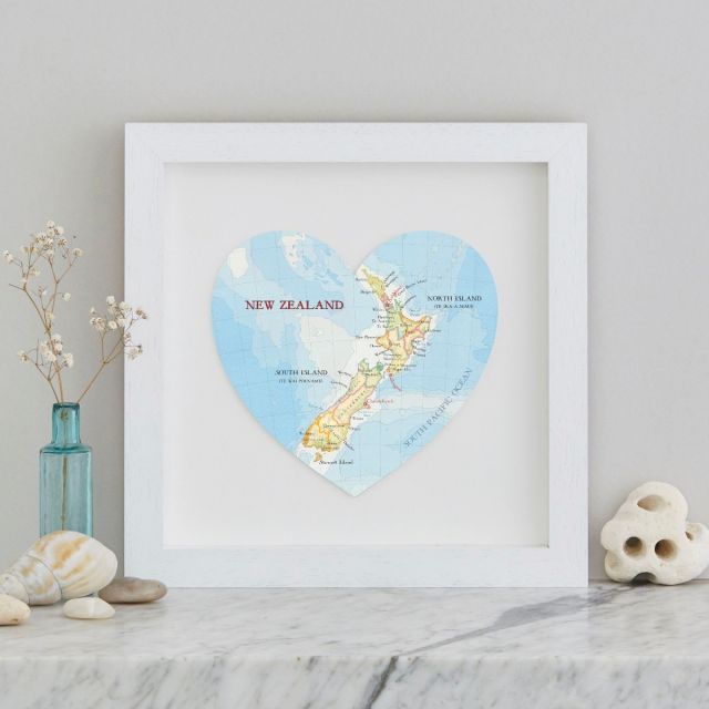 New Zealand map heart in a white frame with gypsum flowers and blue glass bottle, shells and pebbles. Aukland, North Island and Christchurch south island NZ